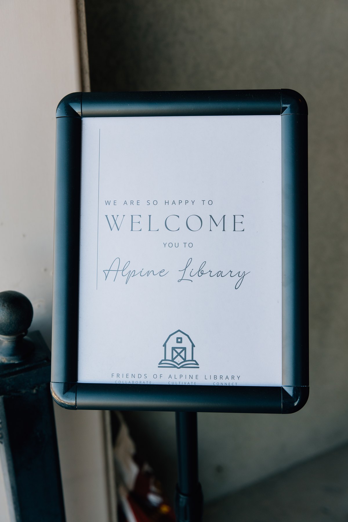 A framed sign reading We are so happy to welcome you to Alpine Library